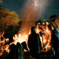 A group of people sitting around a campfire under a night sky filled with stars